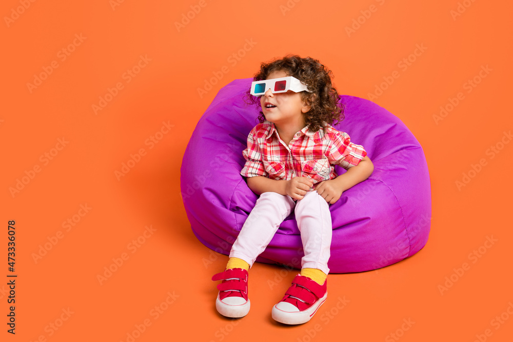 Photo of pretty excited school girl dressed checkered clothes sitting bean bag looking empty space isolated orange color background