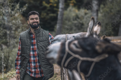 Bearded farmer standing near the donkey in a cattle-pen © zinkevych