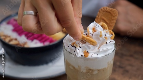 Woman hand tacking a cookie with cream from decoration on her morning coffee in cafe 