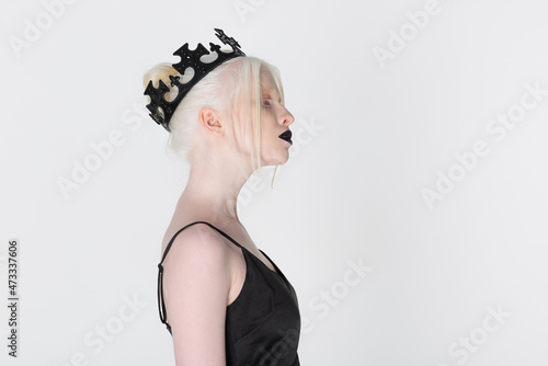 Side view of albino woman in black crown standing isolated on white.