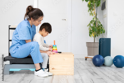 Therapist doing development activities with a little boy with cerebral palsy, having rehabilitation, learning . Training in medical care center. High quality photo. photo