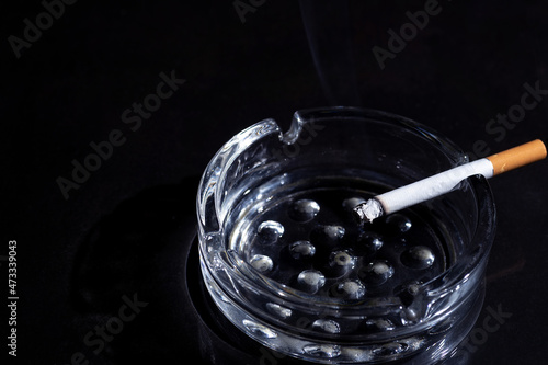 Ashtray and smoking cigarette on black background