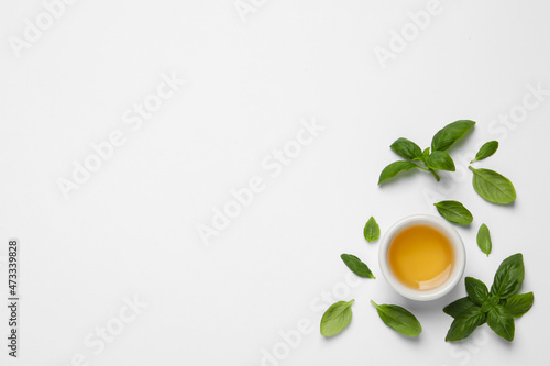 Essential basil oil and fresh leaves on white background, flat lay. Space for text