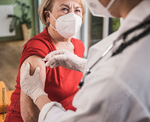 Senior woman with face mask getting vaccinated at home photo