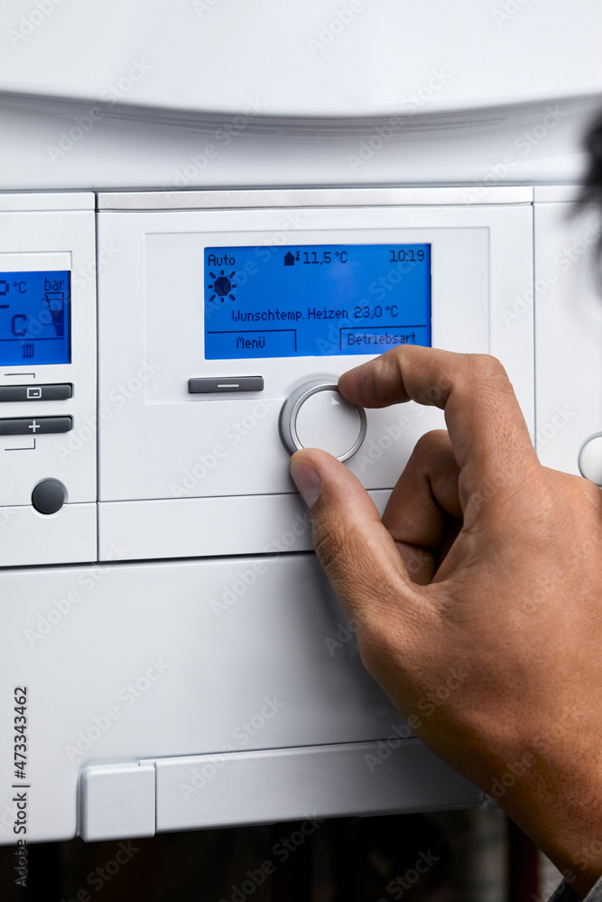 Man adjusting heating boiler with control knob at home Man adjusting heating boiler with control knob at home