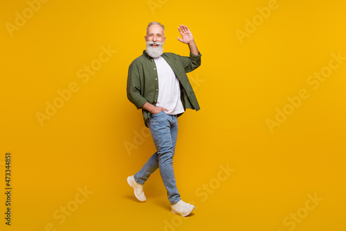 Full length body size photo of positive happy senior man smiling waving hand isolated vivid yellow color background photo