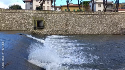 Scorcio del fiume Bisenzio a Prato in Toscana, che scorre e incontrando una piccola chiusa crea schiuma, spruzzi e onde photo