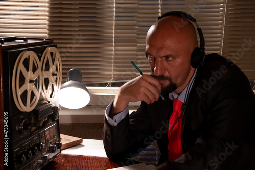 Canvas Print An FBI or KGB secret agent eavesdrops on headphones and records the conversation on a reel-to-reel tape recorder, holding a pencil in his hand