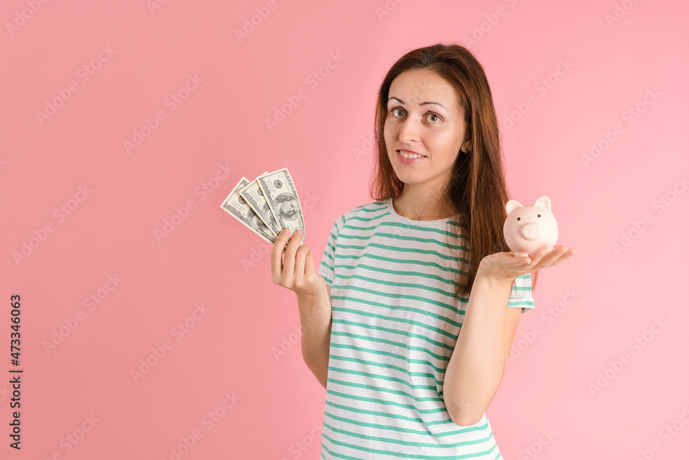 A freelancer girl in casual clothes smiles and holds hundred dollar bills and a piggy bank in her hands standing on a pink background A freelancer girl in casual clothes smiles and holds hundred dollar bills and a piggy bank in her hands standing on a pink background