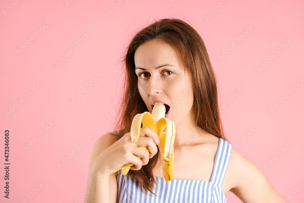 Hungry sexy brunette bites a banana on a pink background Hungry sexy brunette bites a banana on a pink background