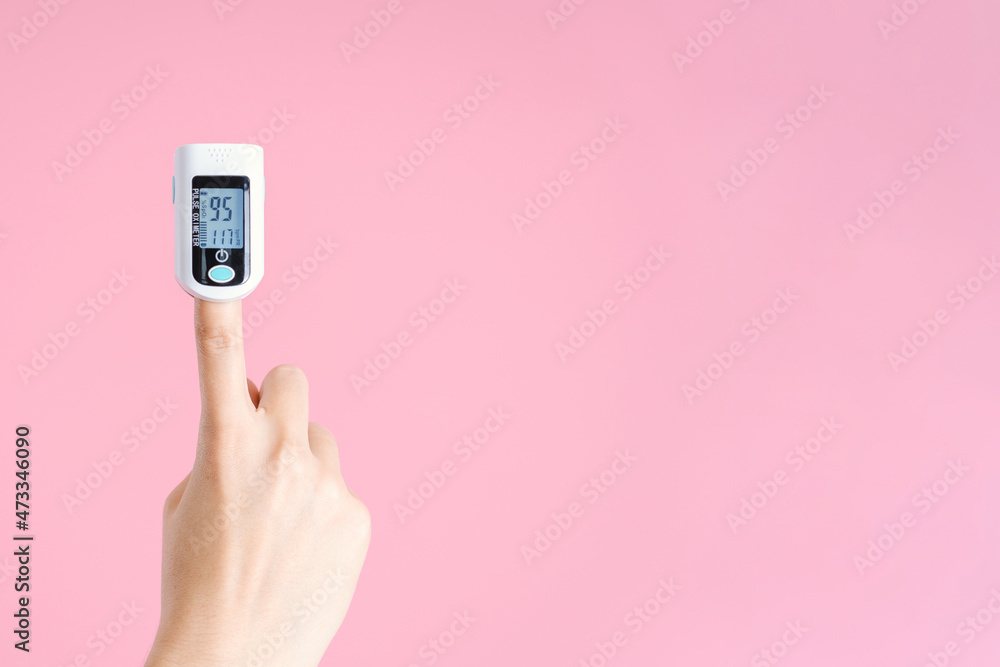 Female hand with pulse oximeter on index finger on pink background. Copy space Female hand with pulse oximeter on index finger on pink background. Copy space