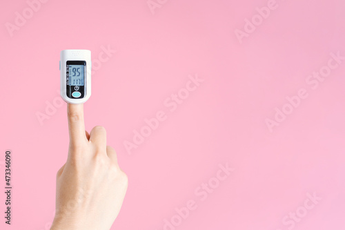 Female hand with pulse oximeter on index finger on pink background. Copy space photo
