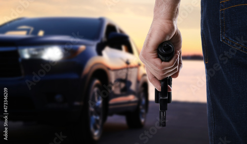 Man with gun near luxury car outdoors, closeup