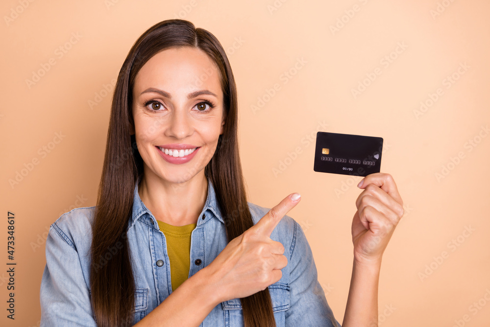 Photo of cheerful woman advertising credit card pointing finger wear casual denim shirt isolated on beige color background Photo of cheerful woman advertising credit card pointing finger wear casual denim shirt isolated on beige color background