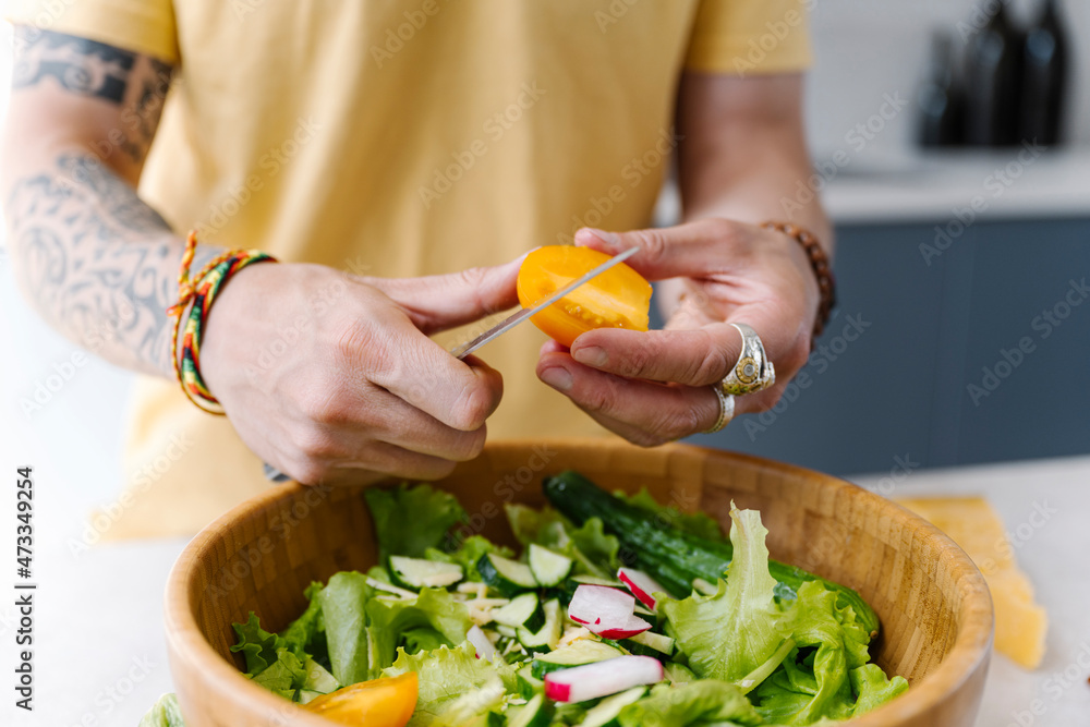 Man cutting yellow tomato while preparing salad in kitchen Man cutting yellow tomato while preparing salad in kitchen