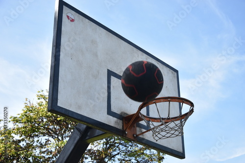 Aro de baloncesto y tablero, de parque con fondo de cielo azul  y balón gastado, con tablero un poco sucio por el uso photo