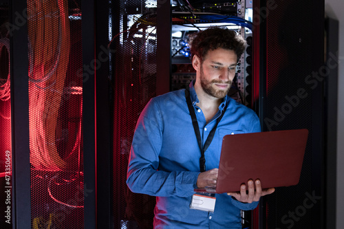 Male engineer working on laptop in server room photo