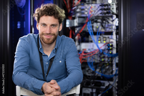 Contented male IT specialist with hands clasped sitting at data center photo