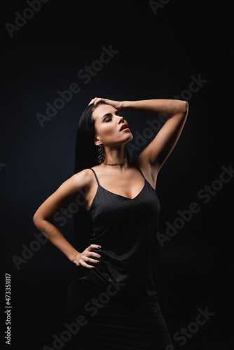 brunette young woman in slip dress posing with hand on hip isolated on black.