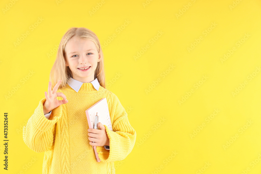 Cute little girl with notebook and pen on yellow background Cute little girl with notebook and pen on yellow background