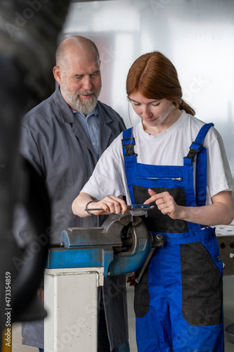 Female apprentice working with machinery while male instructor assisting in workshop photo