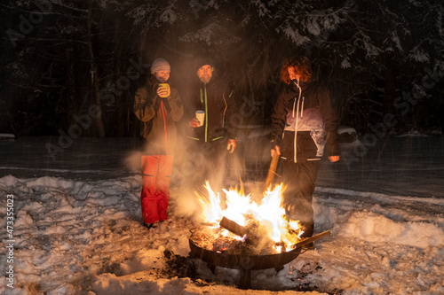 Family standing together around campfire during winter at night photo