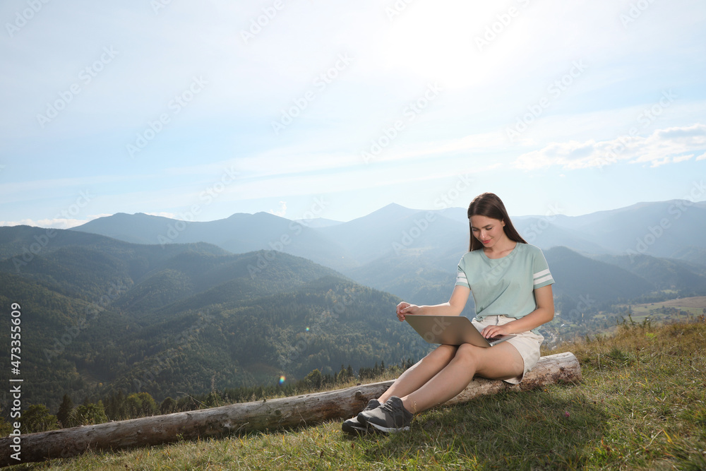 Young woman working with laptop in mountains on sunny day