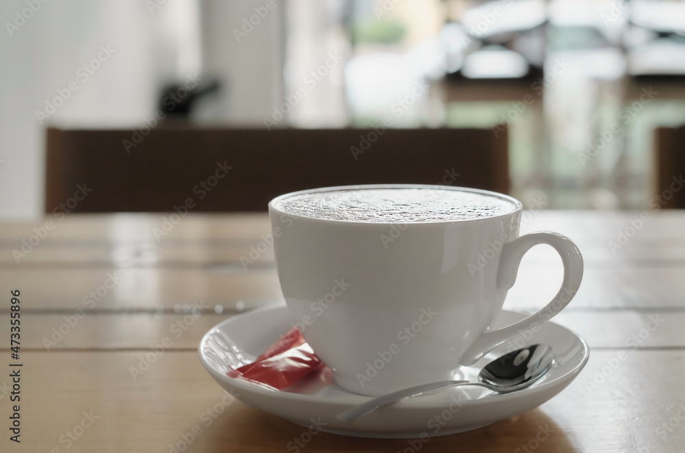 Cappuccino coffee in a white cup on a wooden table. Selective focus on a cup in a cafe with background lighting Cappuccino coffee in a white cup on a wooden table. Selective focus on a cup in a cafe with background lighting