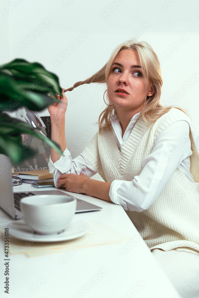 Young girl winds her hair on a finger with a pensive face at a work table Young girl winds her hair on a finger with a pensive face at a work table