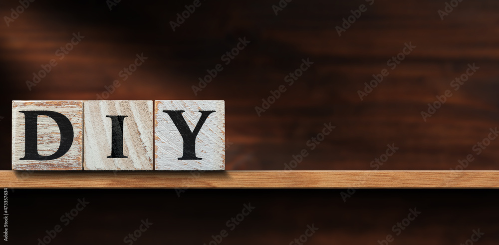 Close-up of text Diy (do it yourself), made of wooden blocks, above a wooden shelf or workbench with copy space.