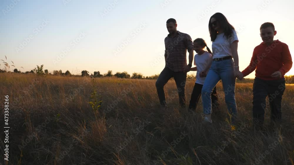 Young couple of parents with small kids walk through grass field holding hands of each other at sunset. Happy family with children going among meadow and enjoy to spending time together. Dolly shot Young couple of parents with small kids walk through grass field holding hands of each other at sunset. Happy family with children going among meadow and enjoy to spending time together. Dolly shot