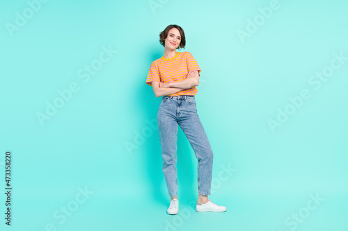 Photo of pretty charming young lady wear orange t-shirt arms folded smiling isolated turquoise color background