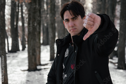 Portrait of a disgruntled man showing thumbs down. The guy is walking on the street.