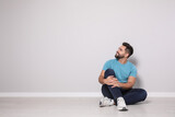 Young man sitting on floor near light grey wall indoors. Space for text