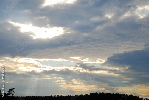 Summer cloudy sky covered with clouds. In the sky, white-gray, slightly blue clouds with white gaps through which the sun's rays break through.