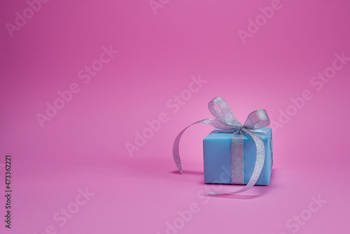 Blue gift box in the snow on a pink background. Christmas background concept with copy space