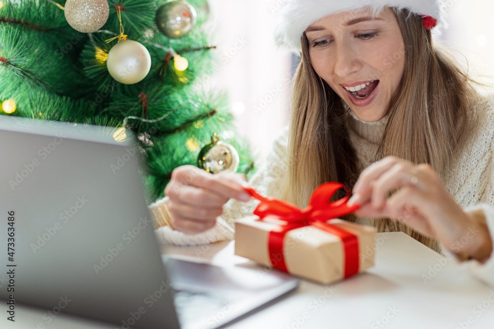 Young woman opening Christmas or new year present when calling to friends via video chat from home Young woman opening Christmas or new year present when calling to friends via video chat from home