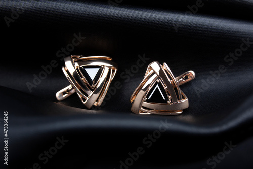 Obraz na plátně Golden earrings with the black stone on black leather background.