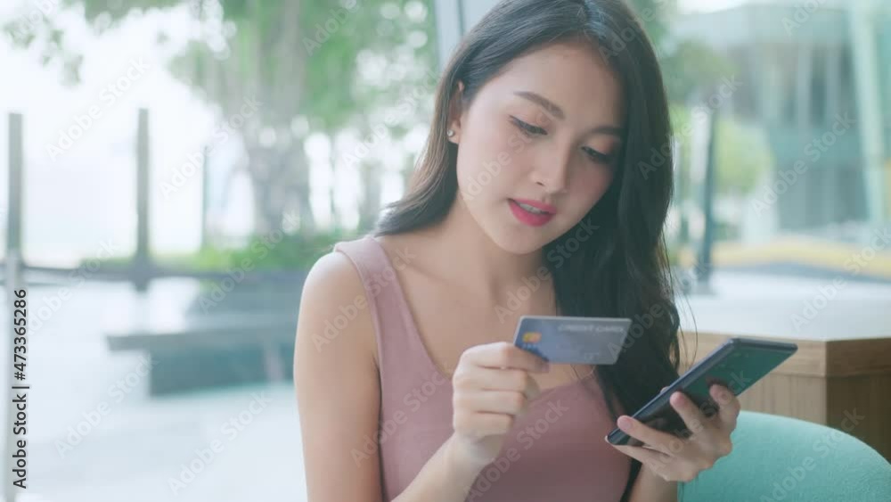 Beautiful asian young female with cheerful expression, holds smart phone and credit card, banks online,Happy young girl holding plastic credit card while using mobile phone at the cafe Beautiful asian young female with cheerful expression, holds smart phone and credit card, banks online,Happy young girl holding plastic credit card while using mobile phone at the cafe