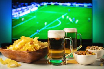 Beer and snacks set on football match tv background