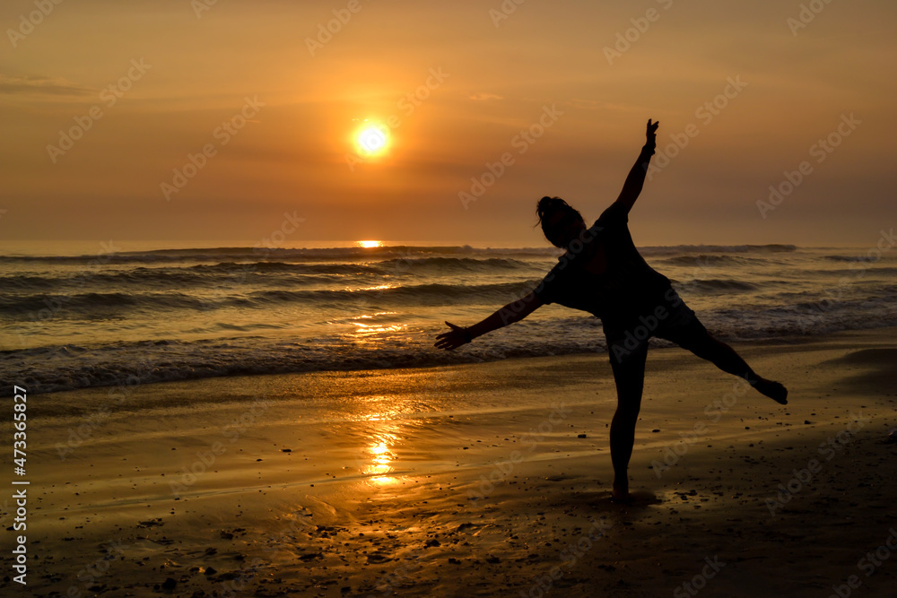 Silhouette of a woman with open arms on the shore of a beach at sunset. The golden hour