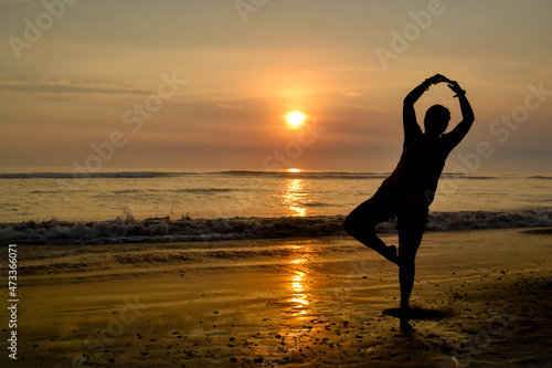 Silhouette of a woman with open arms and on one foot on the shore of a beach at sunset