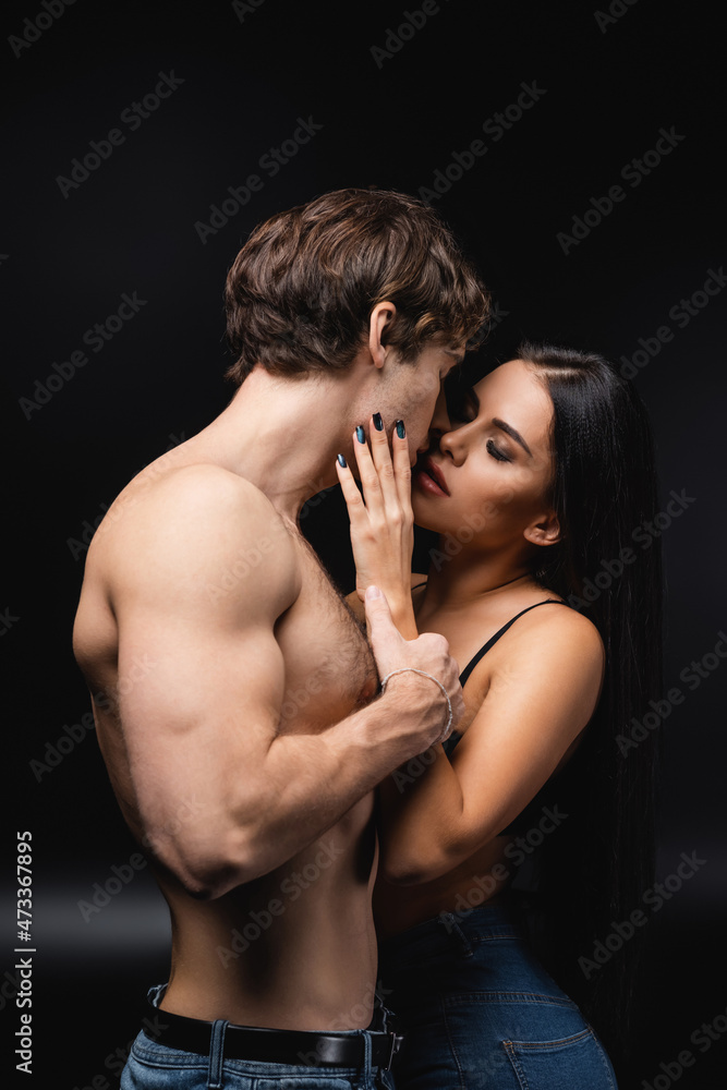 young woman in bra hugging and kissing muscular boyfriend on black. young woman in bra hugging and kissing muscular boyfriend on black.