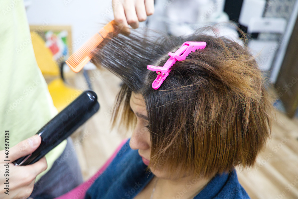 Fototapeta premium Transgender woman combing her hair with hairdryer, comb and hair straightener in the beauty salon by the professional stylist. Concept of beauty and hairdressing. Beauty and health center.