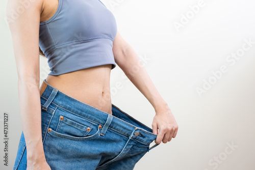 person wearing oversized old jean pants before weight loss success isolated on background. © Pormezz