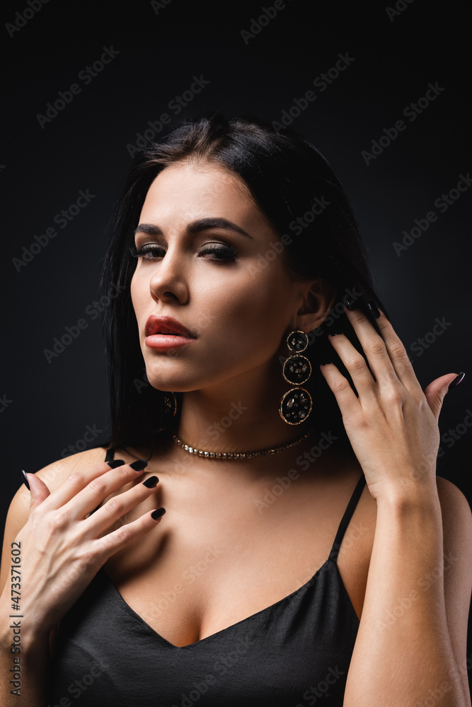 pretty young woman in accessories adjusting hair isolated on black.