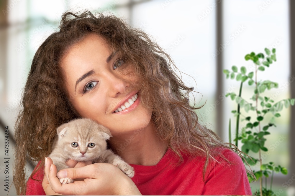 Happy beautiful cheerful young woman with a cute gray cat in her arms at home