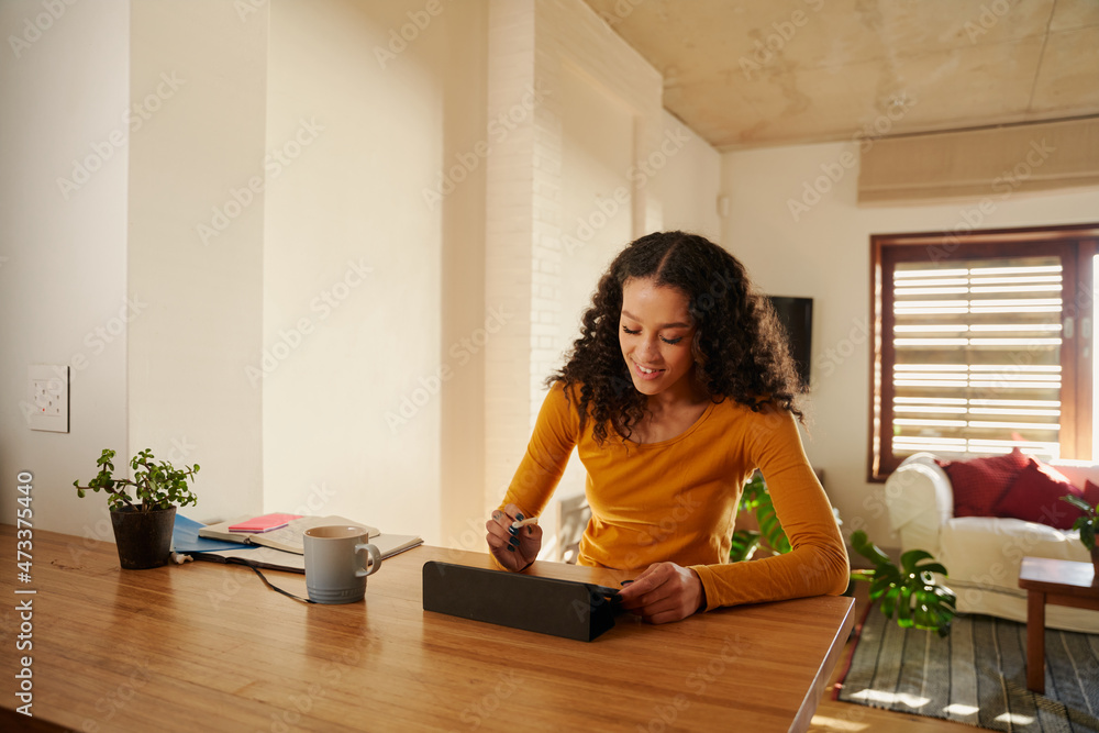 Multi-cultural young adult female smiling while using using her electronic tablet at her modern kitchen counter. Remote working