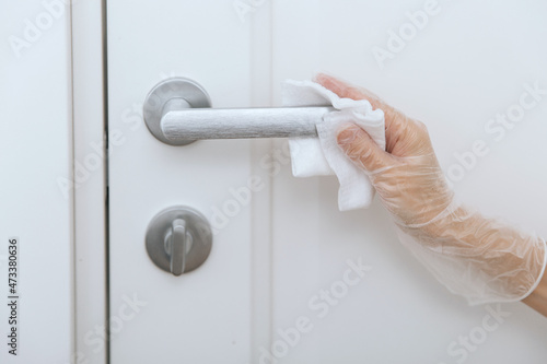 Cleaning door handles with wet wipe and white gloves. Sanitize surfaces prevention in hospital and public spaces against corona virus. Woman hand using towel for cleaning home room door link.