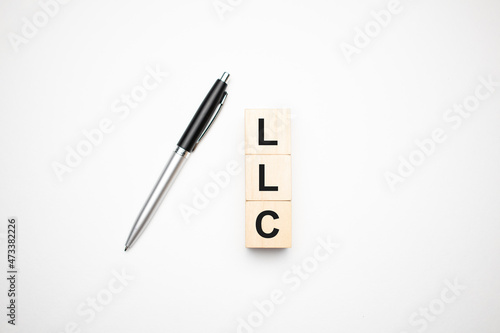 llc is made up of wooden cubes that stand on a burgundy notebook near the pen. Business concept photo